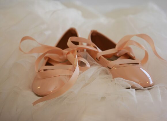 The Affordable And Beautiful Unmentionables: Nude Ballet Flats Pale pink ballet flats with glossy finish and ribbon ties rest on delicate white tulle fabric, conveying an elegant and graceful tone.
