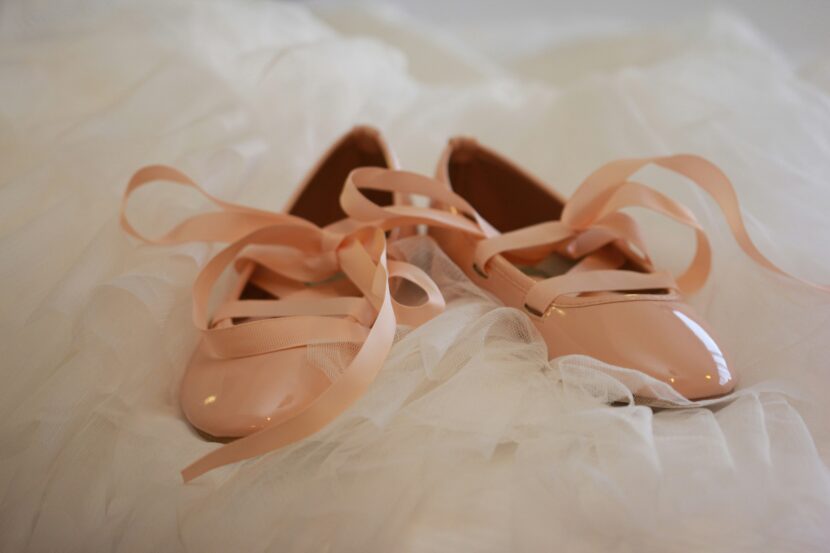 The Affordable And Beautiful Unmentionables: Nude Ballet Flats Pale pink ballet flats with glossy finish and ribbon ties rest on delicate white tulle fabric, conveying an elegant and graceful tone.