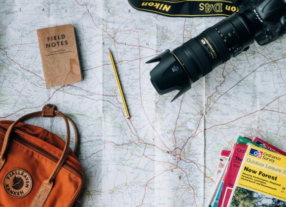 ✈️ Why Birkenstocks Are a Travel Essential A travel-themed flat lay featuring a map, camera, notebook, pencil, orange backpack, and colorful guidebooks, evoking a sense of adventure.
