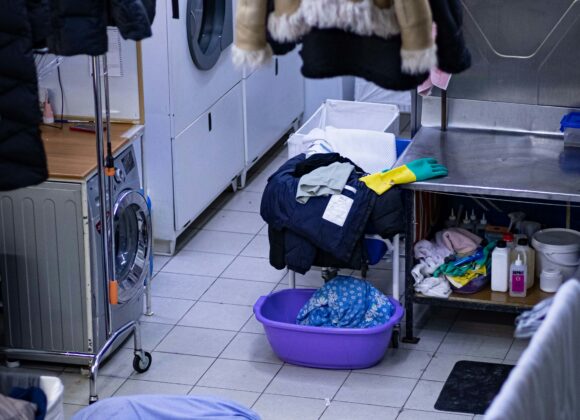 The Dirty Laundry Dilemma No One Talks About A busy laundry room with clothes hanging to dry, washing machines, and a cluttered surface with cleaning supplies. A cozy, functional atmosphere.