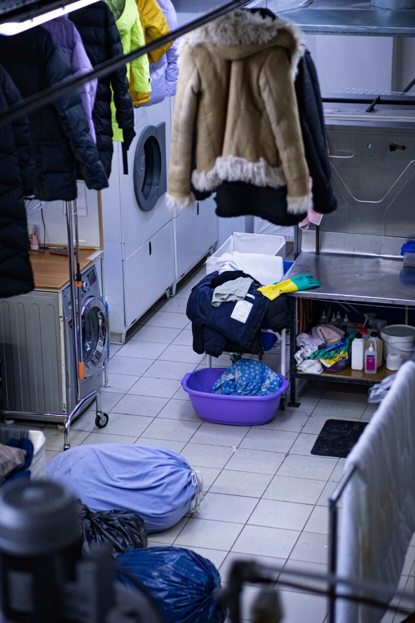 The Dirty Laundry Dilemma No One Talks About A busy laundry room with clothes hanging to dry, washing machines, and a cluttered surface with cleaning supplies. A cozy, functional atmosphere.