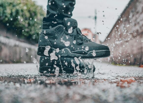 🌧️ Why Waterproof Sneakers Are a Must-Have for Women Close-up of a person wearing black sneakers splashing through a puddle, sending droplets into the air. The street setting conveys a playful, dynamic mood.