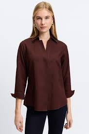 The Ultimate Guide to Women's Wrinkle-Free Shirts A woman with long blonde hair wearing a dark brown blouse and black pants stands against a plain white background, conveying a casual yet polished look.