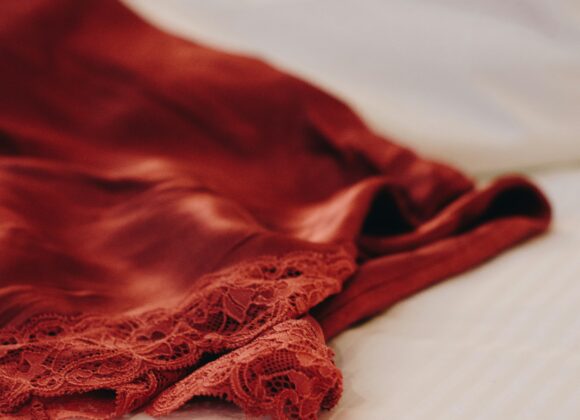 Best Silk Long Underwear: The Ultimate Guide to Staying Warm in Style A silky, red garment with delicate lace trim is casually draped over a bed with white, striped sheets, conveying a sense of elegance and comfort