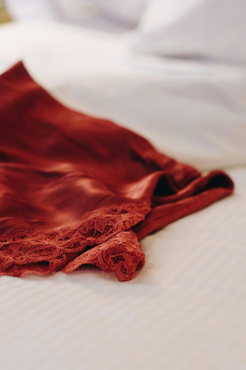 Best Silk Long Underwear: The Ultimate Guide to Staying Warm in Style A silky, red garment with delicate lace trim is casually draped over a bed with white, striped sheets, conveying a sense of elegance and comfort
