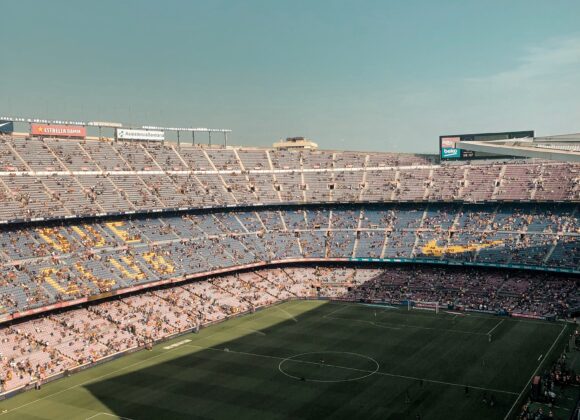 ā½ FIFA World Cup 2026 Tickets: Your Ultimate Guide to Attending the Biggest Football Event in History Aerial view of a large, filled football stadium under a clear sky. The vibrant green pitch contrasts with rows of multicolored seats and cheering fans.
