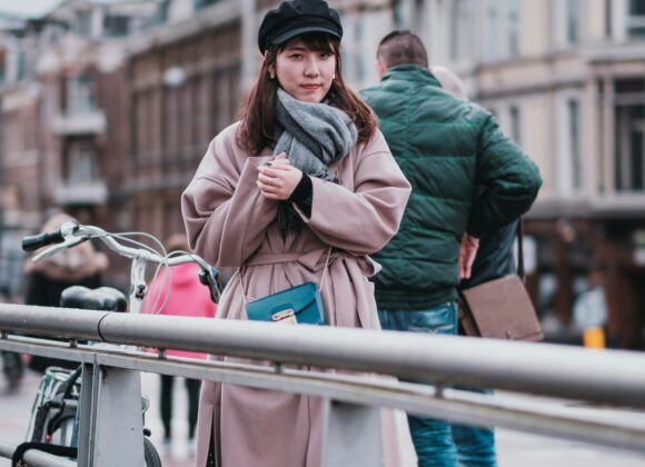 What to Wear in Amsterdam in May: The Complete Traveler’s Guide 1. A woman wearing a coat and hat stands on a bridge, looking out over the water below. 2. A woman in a coat and hat stands on a bridge, with a scenic view of the river and city skyline in the background. 3. A woman dressed in a coat and hat stands on a bridge, gazing thoughtfully at the landscape around her.