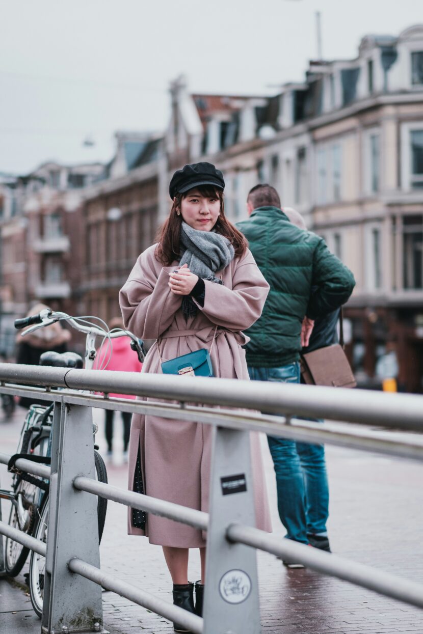 What to Wear in Amsterdam in May: The Complete Traveler’s Guide 1. A woman wearing a coat and hat stands on a bridge, looking out over the water below. 2. A woman in a coat and hat stands on a bridge, with a scenic view of the river and city skyline in the background. 3. A woman dressed in a coat and hat stands on a bridge, gazing thoughtfully at the landscape around her.
