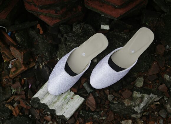 Sorel Shoes for Women: Stylish Comfort That Supports White slip-on shoes with a textured pattern sit on scattered, broken tiles and rocks. The scene conveys a contrast between elegance and decay.