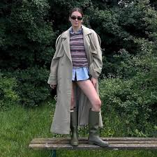 Women’s Waterproof Leather Boots A person poses outdoors on a bench, wearing a long trench coat, striped sweater, shorts, and boots, conveying a stylish, confident vibe. Green trees fill the background.