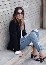 Shoes for Cruise: A Woman’s Guide to Footwear That’s Stylish A woman in sunglasses sits casually on a concrete step. She's wearing a black blazer, white top, ripped jeans, and black heels. The setting is urban and relaxed.