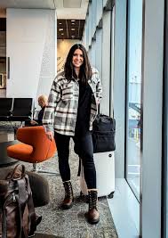 10-Step Packing Guide for Ireland A woman in a checkered jacket and boots smiles while leaning on a suitcase in a modern airport, conveying a sense of adventure and excitement.