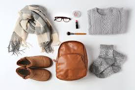 What to Bring to Italy: Winter Edition Alt text: "Flat lay of cozy winter essentials: plaid scarf, gray sweater, knitted socks, brown leather bag, boots, glasses, lipstick, brush, and a small case."