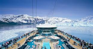 What to Pack for an Alaska Cruise in AugustThe Ultimate Guide Cruise ship deck with a pool, surrounded by passengers, sails through icy waters with snow-capped mountains under a clear blue sky. Scenic and calm.