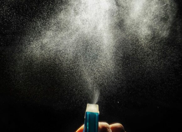 💧 Introduction: Why Waterproof Spray Is a Must-Have A hand presses a blue spray bottle against a dark background, releasing a fine mist that forms a cloud-like pattern, illuminated by light, evoking a sense of calm.
