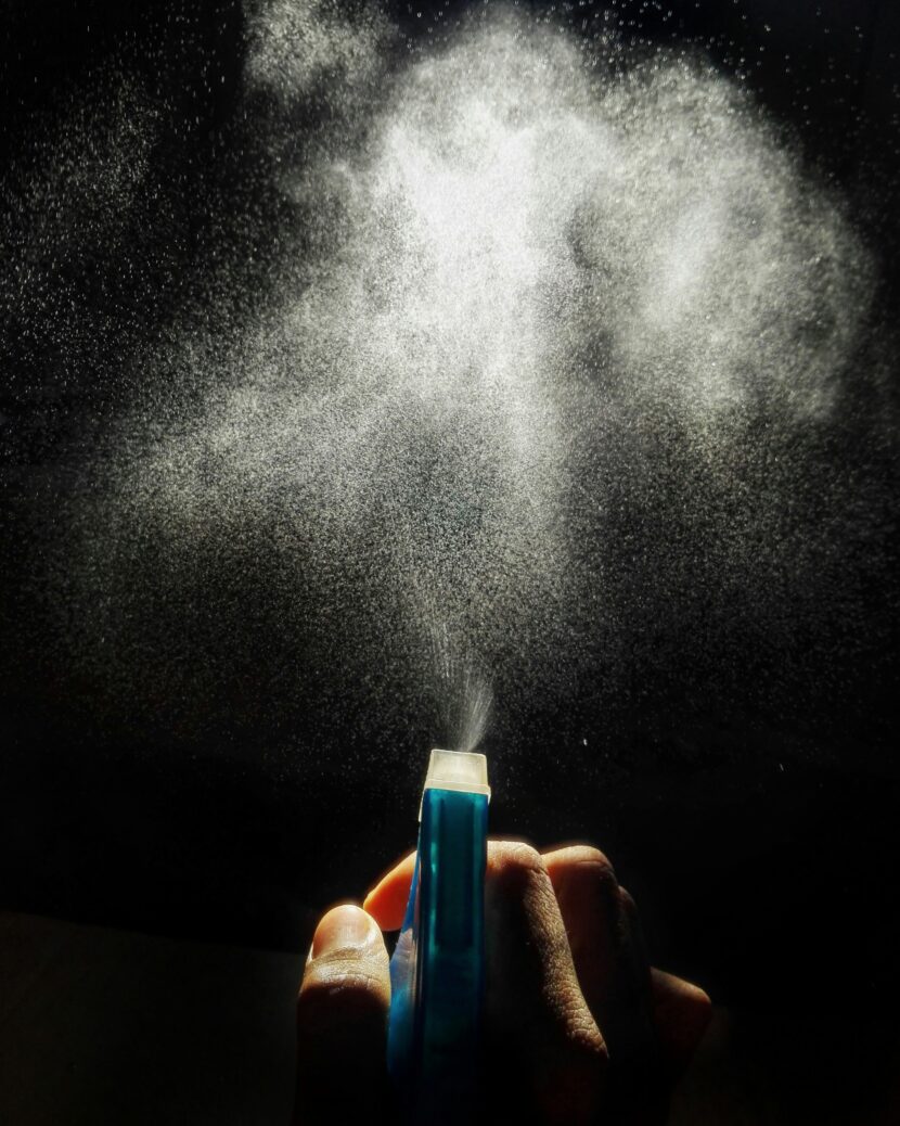 💧 Introduction: Why Waterproof Spray Is a Must-Have A hand presses a blue spray bottle against a dark background, releasing a fine mist that forms a cloud-like pattern, illuminated by light, evoking a sense of calm.