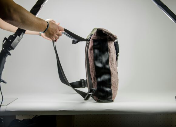 Best Anti-Theft Backpack for Women A person in a studio adjusts a brown and black shoulder bag. The scene is well-lit with a white background, conveying a professional and neutral tone.