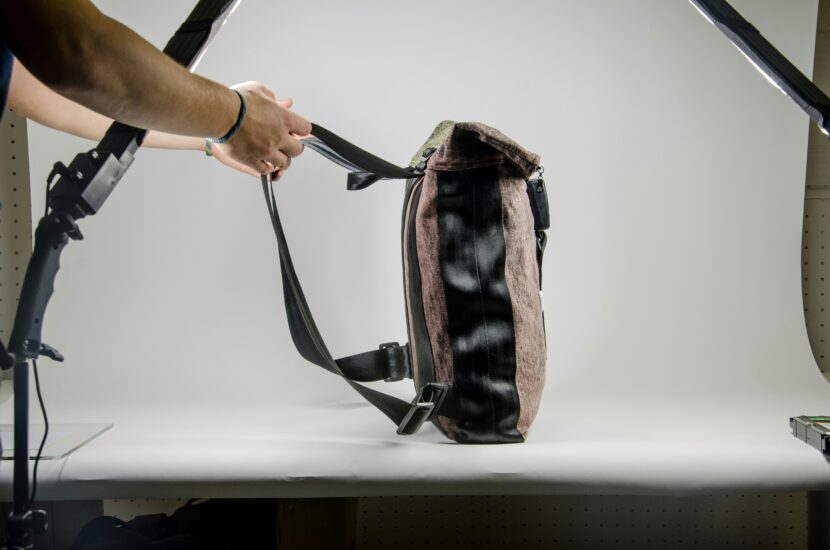 Best Anti-Theft Backpack for Women A person in a studio adjusts a brown and black shoulder bag. The scene is well-lit with a white background, conveying a professional and neutral tone.