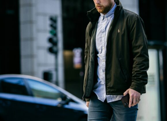 👖 Best Denim Jacket for Women: Top Lightweight Jean Jacket Picks for Every Style A man wearing a jacket and jeans crosses a city street, holding a phone. He appears focused and thoughtful. A blurred car and building are in the background.
