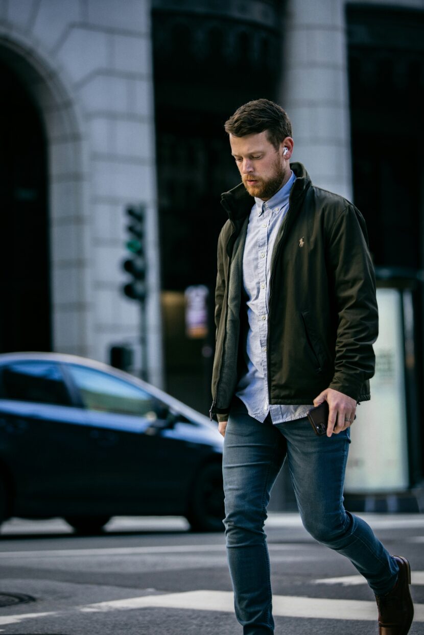 👖 Best Denim Jacket for Women: Top Lightweight Jean Jacket Picks for Every Style A man wearing a jacket and jeans crosses a city street, holding a phone. He appears focused and thoughtful. A blurred car and building are in the background.
