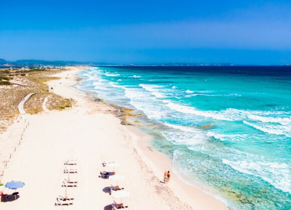 🌴 Beach Vacation Packing List for Mexico: From Inspiration to Reality A sunlit beach with pristine white sand extends towards the horizon, bordered by turquoise waves. Sun loungers and umbrellas create a relaxing, serene atmosphere.