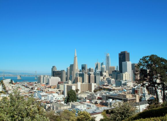 What to Wear in San Francisco (All Seasons) + What to Wear in September A clear view of the San Francisco skyline on a sunny day, featuring the iconic Transamerica Pyramid. The scene includes blue skies and surrounding architecture.