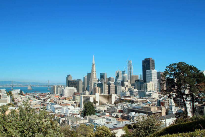 What to Wear in San Francisco (All Seasons) + What to Wear in September A clear view of the San Francisco skyline on a sunny day, featuring the iconic Transamerica Pyramid. The scene includes blue skies and surrounding architecture.