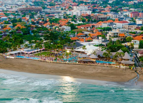 Beach Vacation Packing List for Mexico: From Inspiration to Reality Aerial view of a vibrant beach resort with turquoise pools and palm trees, adjacent to a bustling town with red-roofed buildings and lush greenery.