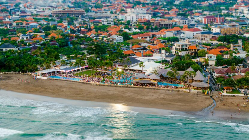 Beach Vacation Packing List for Mexico: From Inspiration to Reality Aerial view of a vibrant beach resort with turquoise pools and palm trees, adjacent to a bustling town with red-roofed buildings and lush greenery.