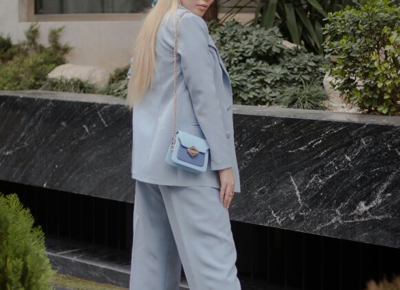 🌧️ Introduction: Fashion Meets Function in the Blondo Villa Bootie A person in a light blue suit and white sneakers stands outside. They wear a colorful headscarf and carry a matching light blue purse, exuding confidence.