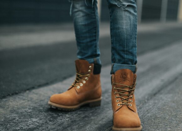 👢 Best Mid-Calf Boots for Women: Style Guide for Pairing Jeans with Mid-Calf Boots A person wearing distressed jeans and tan work boots stands on a dark, textured road. The background features blurred garages, creating an urban feel.