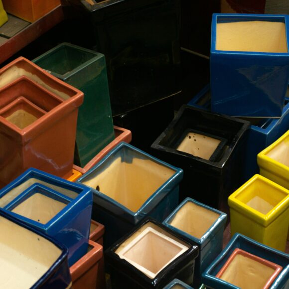A collection of colorful, glossy, square-shaped ceramic pots stacked together. They vary in size and include hues such as red, blue, green, and yellow.