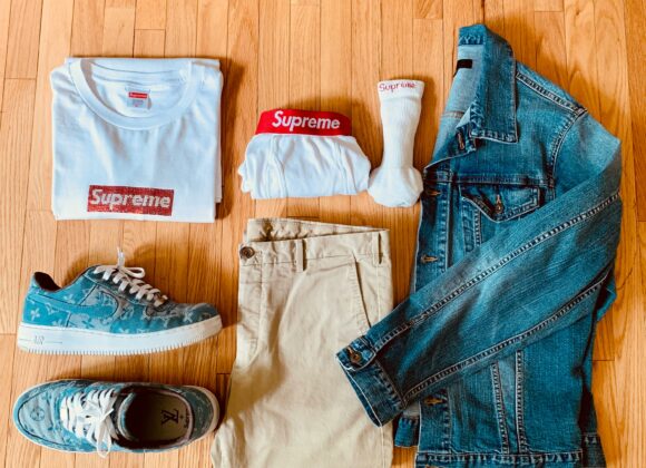 The Only Packing & Outfit Guide You’ll Need Casual outfit on wood floor: folded white Supreme t-shirt, red-banded briefs, socks, denim jacket, khaki pants, and blue sneakers with a graphic print.