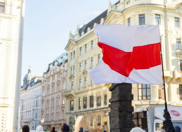 Poland–Russia Relations in 2025: Tensions, Drones, and the NATO Dilemma White-red-white flag waved in a city square, surrounded by historic European buildings under a clear sky. Creates a feeling of unity and protest