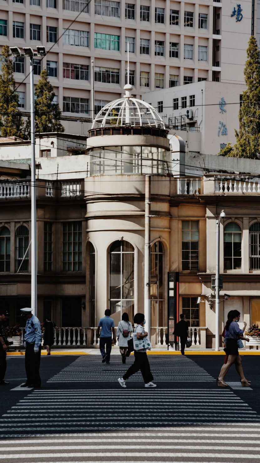 A Glimpse into Buenos Aires Style People cross a city street at a zebra crossing in front of an ornate building with a domed roof. The scene is busy yet calm, set against tall trees and a modern high-rise.