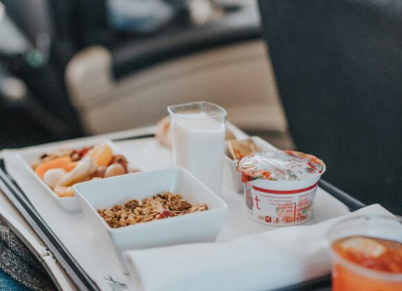 โ๏ธ Best Snacks for Flights That Keep You Full and Happy Airplane tray with breakfast items, including granola, yogurt, juice, and a glass of milk, set on a passenger's tray table. Cozy travel ambiance.