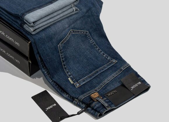 Pacific Coast Highway Road Trip: The Ultimate Guide (Styled with Specific Coast Jeans) Dark blue jeans with a visible pocket and folded cuffs lie over black boxes. Tags displaying a brand name hang from the belt loop, indicating a stylish, casual vibe.