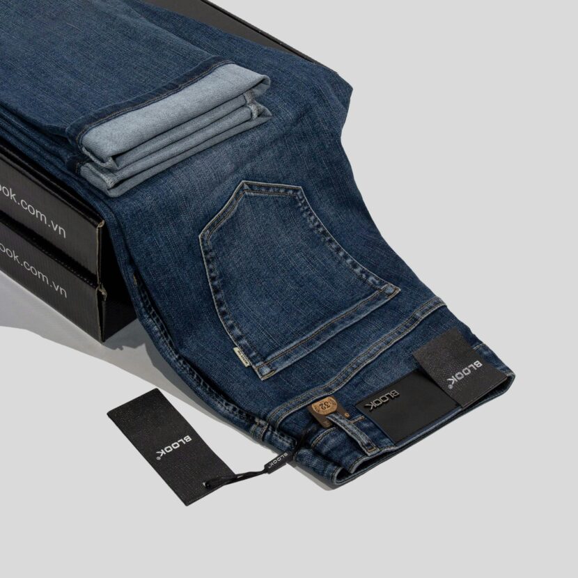Pacific Coast Highway Road Trip: The Ultimate Guide (Styled with Specific Coast Jeans) Dark blue jeans with a visible pocket and folded cuffs lie over black boxes. Tags displaying a brand name hang from the belt loop, indicating a stylish, casual vibe.