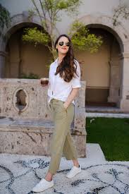 Women's Cropped Pants A woman in sunglasses, wearing a white shirt and beige pants, stands confidently outdoors near a stone bench and lush greenery in a sunny setting.