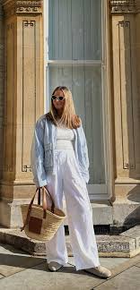 🌿 White Linen Women’s Trousers Woman in a light blue denim jacket and white pants stands confidently outdoors. She carries a straw tote and wears sunglasses, exuding a casual, stylish vibe.