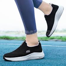 Women’s Skechers Shoes Person walking on a blue track wearing black slip-on athletic shoes with white soles and purple leggings, conveying movement and outdoor activity.