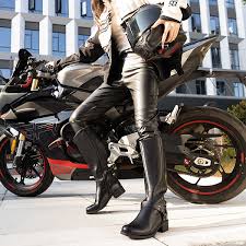 The Best Women's Motorcycle Boots for Every Journey A person in stylish motorcycle gear stands next to a sleek black motorcycle on a sidewalk. Modern building in the background; confident and dynamic mood.