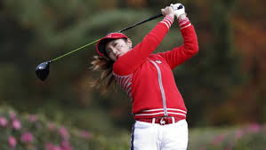 Women's Golf Skirts: Where Style Meets Swing Golfer in red attire swings a club on a lush course, with blurred green and floral background, conveying focus and determination.