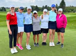 Women's Golf Shirts: Where Style Meets Performance Seven women wearing golf attire and caps stand on a lush golf course. They smile and pose arm-in-arm, conveying camaraderie and joy.