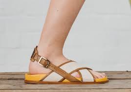 Wide-Width Sandals for Women A close-up side view of a foot wearing a sandal, featuring brown leather straps and a yellow sole, on a wooden surface against a light grey background.