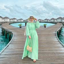What to Wear in the Maldives: Your Ultimate Style Guide Woman in a mint green dress poses on a wooden boardwalk over turquoise water, surrounded by overwater bungalows, with a cloudy sky overhead.